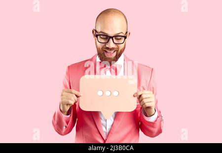 Positive funny man holding bubble talk sign with three dots isolated on pastel pink background. Stock Photo