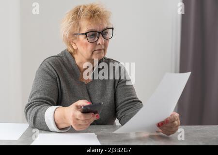 An elderly woman fills a receipt for payment of utility bills. Stock Photo