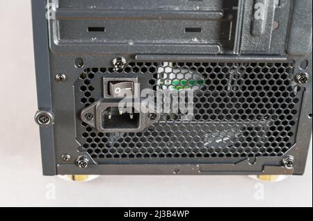 The back of a personal computer system unit. Black metal case with ventilation grille. Close-up of the power switch and power cord socket. Modern digi Stock Photo