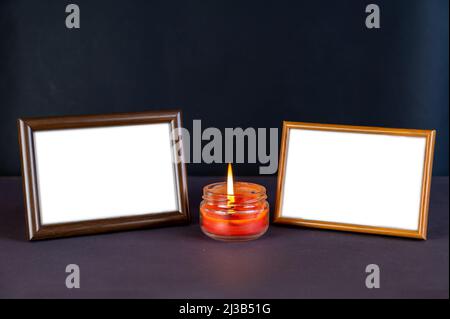 Two Empty Photo Frames against the black damaged area next to the burning candle. Red wax lit candle in a clear glass jar. Horizontally arranged woode Stock Photo