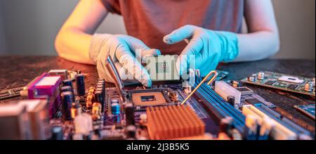 The engineer's gloved hand is holding the CPU chip against the background of the motherboard. Concept of high-tech hardware microelectronics Stock Photo