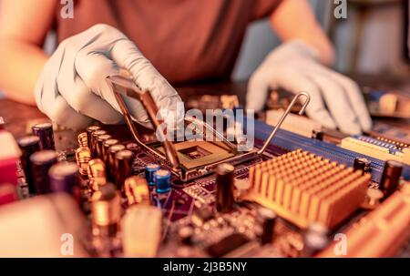 Engineer repairman holding hands in black gloves chip processor, CPU to insert into the socket of the computer motherboard. The concept of technology Stock Photo
