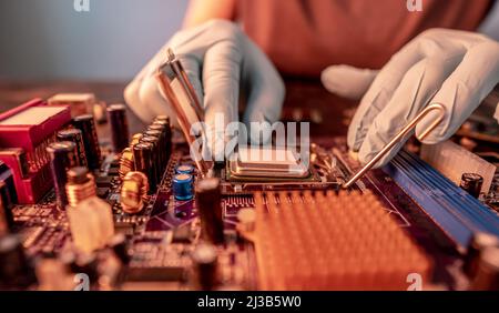 The engineer's gloved hand is holding the CPU chip against the background of the motherboard. Concept of high-tech hardware microelectronics Stock Photo