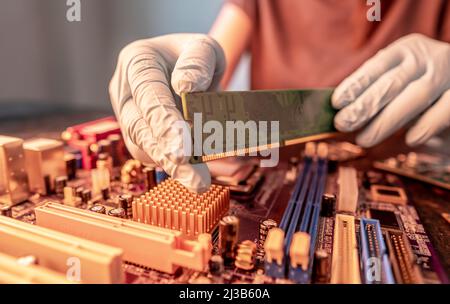 A repair engineer holds a RAM chip with his hands in black gloves, inserts the computer's RAM into the socket of the computer's motherboard. The conce Stock Photo