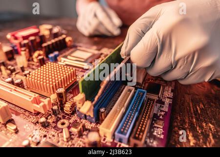 A repair engineer holds a RAM chip with his hands in black gloves, inserts the computer's RAM into the socket of the computer's motherboard. The conce Stock Photo