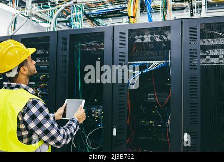 Young technician man working with tablet inside big data center room - Focus on face Stock Photo