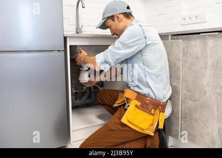 The master in the form makes installation or dismantling of a water pipe or installs a mixer in the kitchen Stock Photo