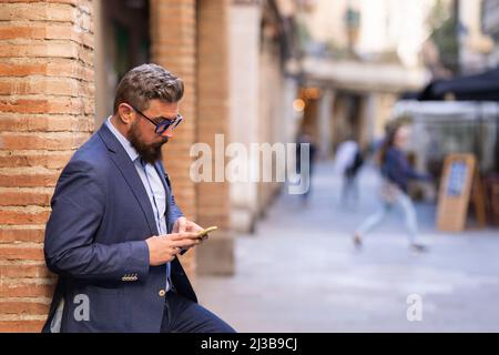 Adult man leaning on column using his phone outside Stock Photo
