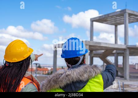Structural engineer and foreman worker  in orange and yellow vests and hard hats discussing the plan working for the outdoors building construction si Stock Photo