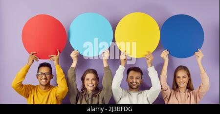 Colored round speech bubbles with copy space in hands of happy young people on purple background. Stock Photo