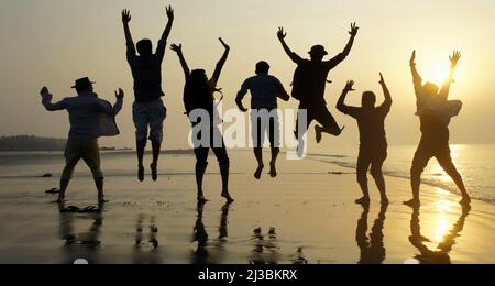 Big group of seven happy friends is having fun and jumping on beach during sunset time at Kuakata sea beach, Bangladesh Stock Photo