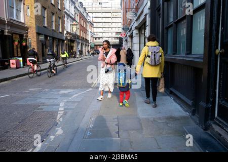 Rear back view of mother holding child's hand walking along street back home after picking up from school in City of London UK  KATHY DEWITT Stock Photo