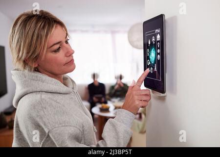 Woman using smart home application on wall mounted tablet Stock Photo