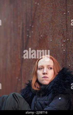Young woman sitting against wall Stock Photo
