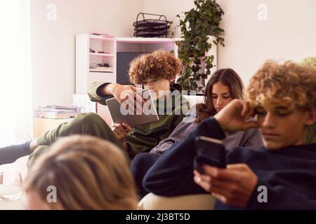 Siblings using electronic devices at home Stock Photo