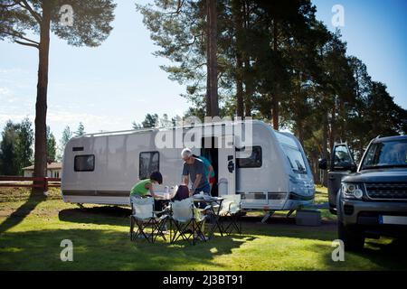 Family having meal in front of camper trailer Stock Photo
