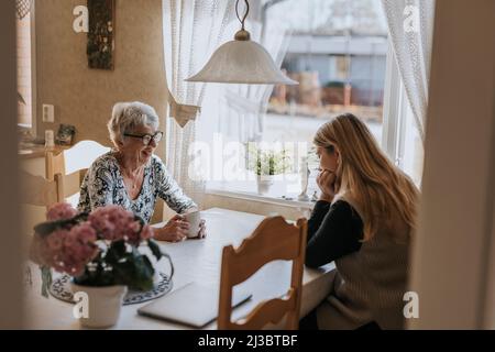 Grandmother and adult granddaughter sitting at table and having tea Stock Photo