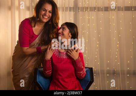 Young girl sitting on chair and mother standing behind with her hands on daughter's shoulder Stock Photo