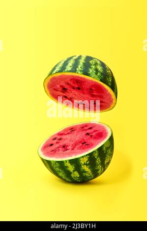 Ripe watermelon cut in half flying in the air on yellow background Stock Photo