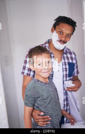 Portrait of happy young father shaving with little boy imitating dad ...