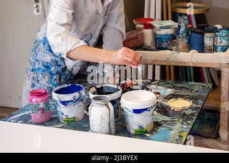 Close up of painter hands squeezing paint from tube on table wearing white coat covered with splashes of paint Stock Photo