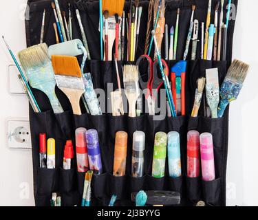 Closeup of colorful dirty paintbrushes, markers and other artistic tools organized in black holder on the white wall Stock Photo