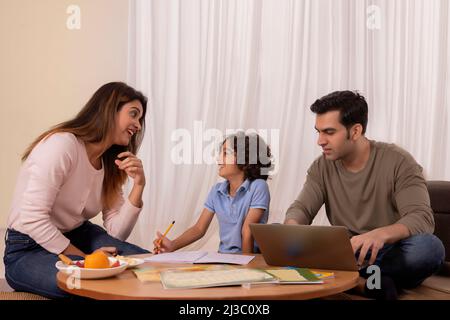 Mother helping son with his homework and father using laptop Stock Photo
