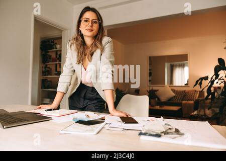 Professional designer working in her home office. Young businesswoman looking at the camera while standing behind her creative desk. Female designer p Stock Photo