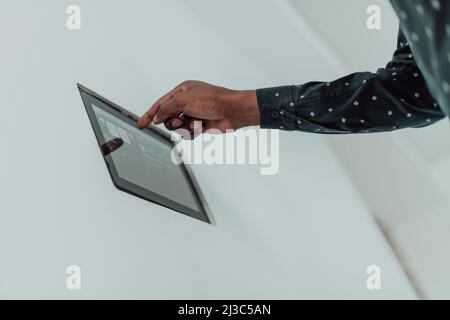 Smiling African American man using modern smart home system, controller on wall, positive young man switching temperature on thermostat or activating Stock Photo