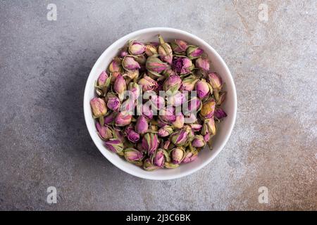 Top view of white bowl with dried rose buds for fragrant tea on grey concrete background Stock Photo