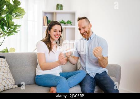 family happy with pregnancy test with his excited wife sitting on a couch at home. Stock Photo