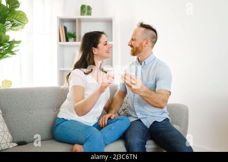 family happy with pregnancy test with his excited wife sitting on a couch at home. Stock Photo