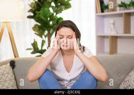 woman feels pain in head sit on sofa Stock Photo