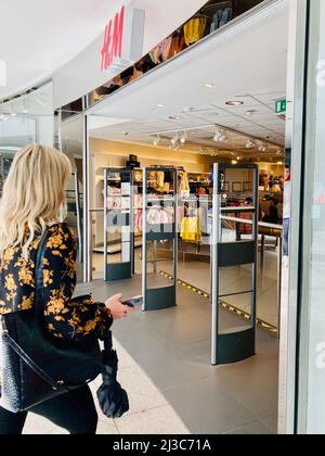 A blonde woman walking through the entrance of H&M high street fashion shop in Leeds Trinity Shopping Centre, UK. Stock Photo