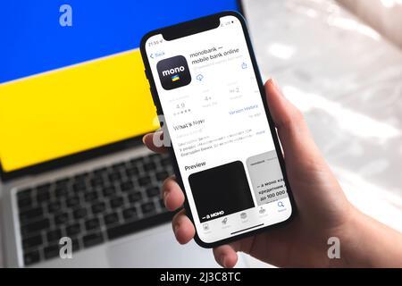 Poltava, Ukraine - April 7, 2022: Monobank mobile banking app in Ukraine. Hand with smartphone, logo on the screen. Background with national flag phot Stock Photo