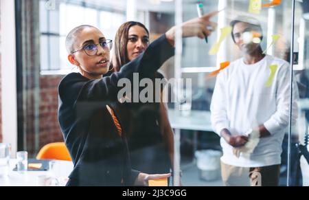 Smart businesswoman sharing her ideas with her team. Confident young businesswoman sharing her sticky notes with her colleagues while standing in fron Stock Photo