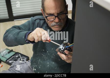 Mature electrician installing power socket with screwdriver. Stock Photo