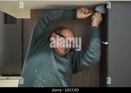 Mature man making a effort to install corner socket with screwdriver. Stock Photo