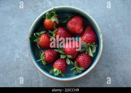 Red fresh strawberries with green leaves in plate on gray background. Top view Stock Photo