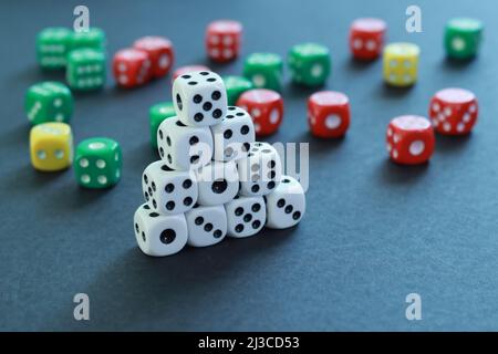 Playing dice mounted in a pyramid and others of several colors in the background on a table Stock Photo