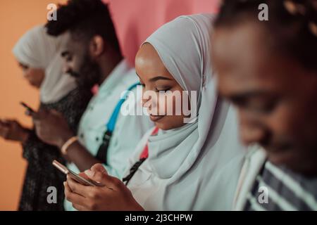 A group of African Muslim students use smartphones while standing in front of a yellow background Stock Photo