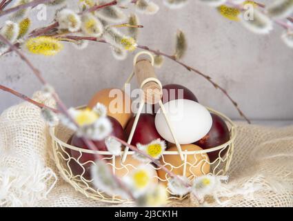 Easter colored eggs and natural eggs lie in a small basket decorated with willow branches. Stock Photo