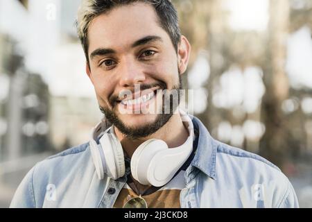 Young hispanic man having fun listening music with headphones with city on background - Focus on face Stock Photo