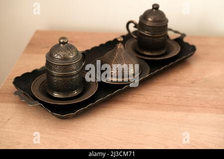 Bronze carved Turkish Coffee mugs on a tray and wooden table Stock Photo