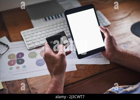 Well deliver right to your desk. Shot of an unidentifiable programmer holding his credit card while using his tablet in the office. Stock Photo