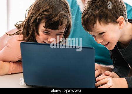 Cropped unrecognizable grandfather with cheerful children watching interesting video on netbook while sitting at table in light room at home Stock Photo