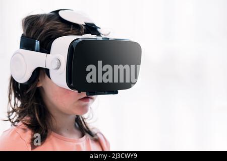 Cute girl in modern wireless VR goggles experiencing virtual reality while standing in light room on white background at home Stock Photo