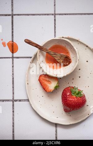 Top view of plate with ripe strawberries and bowl of sweet jam with spoon placed on tiled table in kitchen Stock Photo