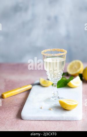Glass chalice of citrus cocktail with sugar rim placed on marble board near knife and cut lemons in daytime Stock Photo