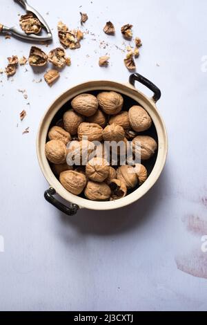 Top view of saucepan with bunch of raw walnuts placed on gray table near nutcracker and nutshells Stock Photo